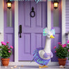 A white lawn goose statue wearing a purple mermaid bikini costume standing in front of a purple door.