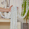 A hand is pulling a white bohemian tassel curtain with lanterns for doorways and windows.