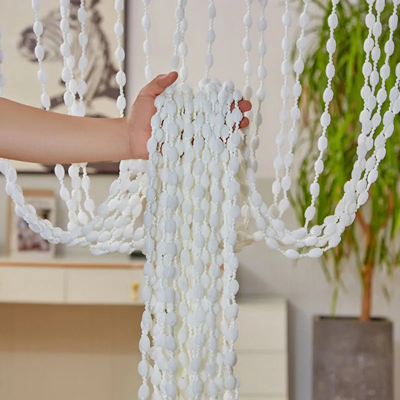 A hand is pulling a white bohemian tassel curtain with lanterns for doorways and windows.