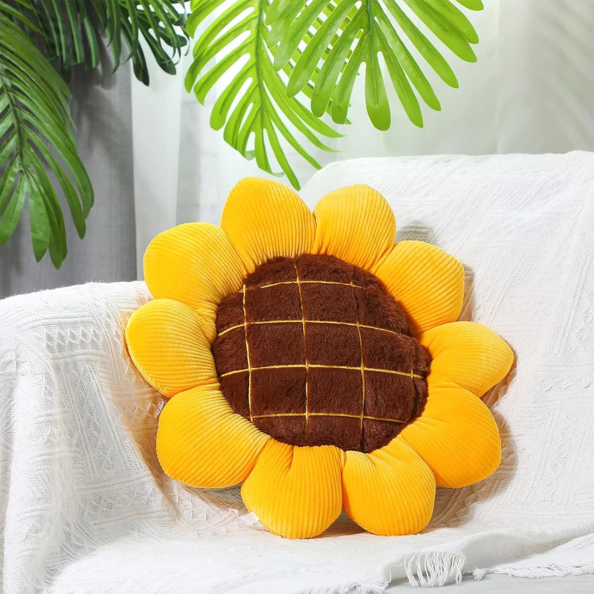 A bright yellow and brown sunflower shaped floor pillow resting on a white textured cloth.