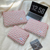 A floral printed laptop sleeve with a red and green pattern is shown resting on a cream-colored fabric.