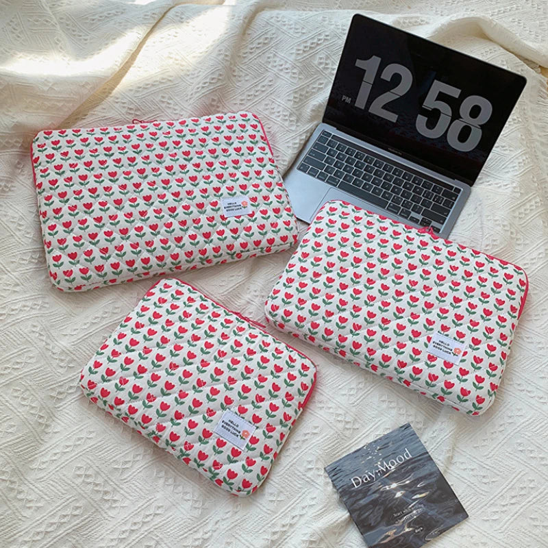 A floral printed laptop sleeve with a red and green pattern is shown resting on a cream-colored fabric.