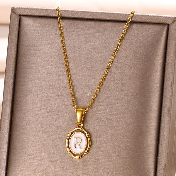 Goldkette mit Anhänger, weißer Initialbuchstabe R in goldenem Rahmen, in einer Schachtel präsentiert.