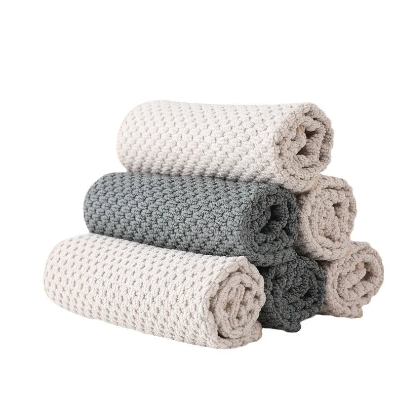A stack of six light beige and gray waffle weave microfiber kitchen towels rolled up.