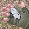 A hand holds a stainless steel folding utility knife with five replaceable blades against a green fabric glove outdoors.