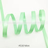 A strand of mint green satin ribbon is shown coiled and unwound against a white background.