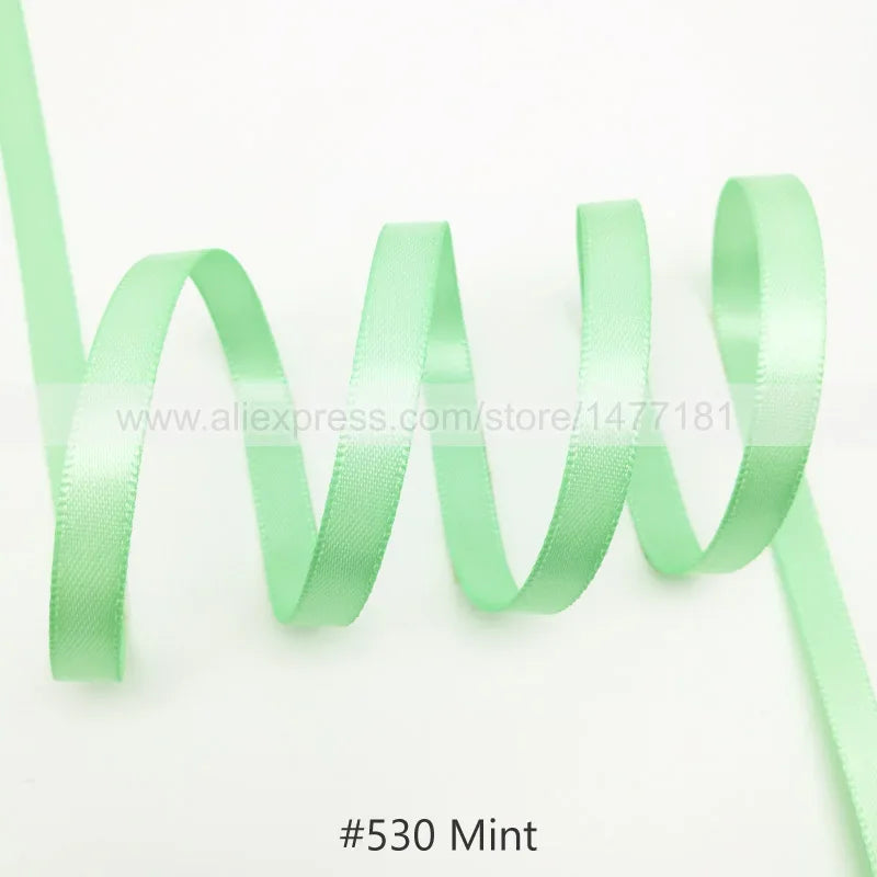 A strand of mint green satin ribbon is shown coiled and unwound against a white background.
