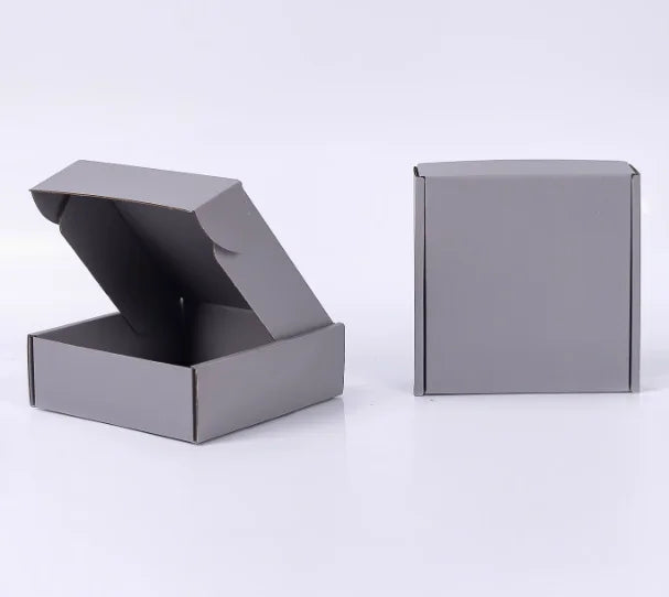 Eine graue Wellpappkartons verpackte Box, offen, mit einer geschlossenen Box daneben.
