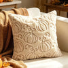 A cream-colored plush throw pillow with an embossed pumpkin pattern rests on a light sofa next to a golden throw blanket.