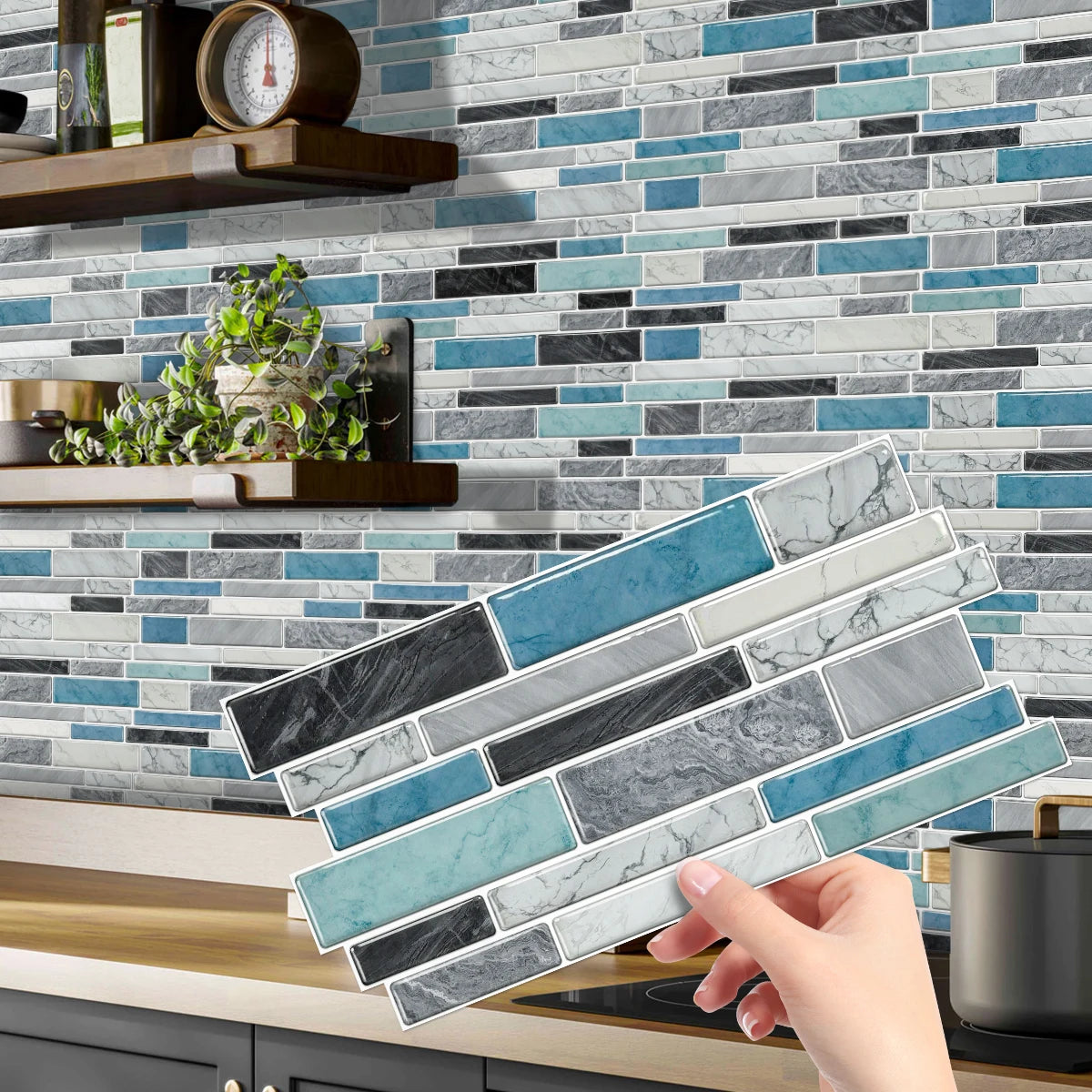 A hand is placing rectangular blue and gray peel-and-stick tile stickers onto a kitchen backsplash.