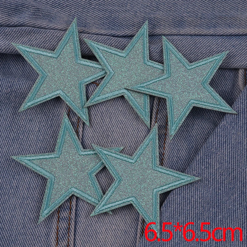 A set of five teal glitter star iron-on embroidered patches placed on a denim fabric background.