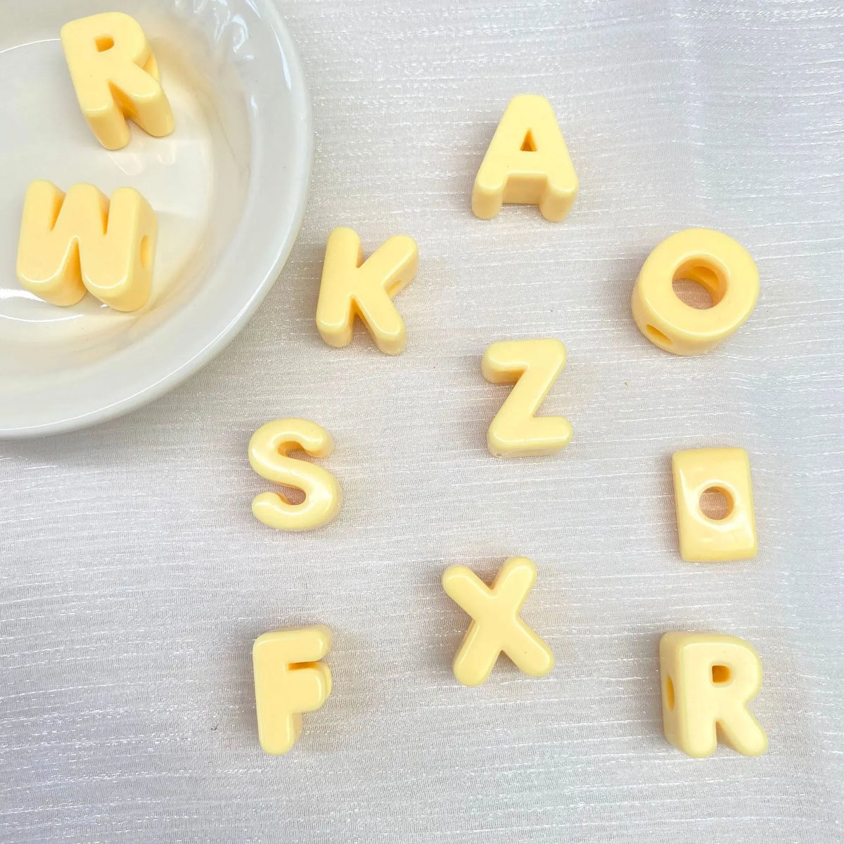 Perles en acrylique jaunes formant les lettres R W K Z S O X F R, éparpillées sur une surface blanche