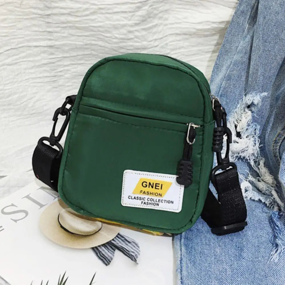 A dark green mini canvas crossbody bag with black strap resting on a light background.
