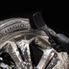 A hand uses a black brush to clean white foam from a silver alloy wheel rim.