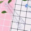 A transparent foldable plastic ruler with markings is displayed on a pink and white grid background.