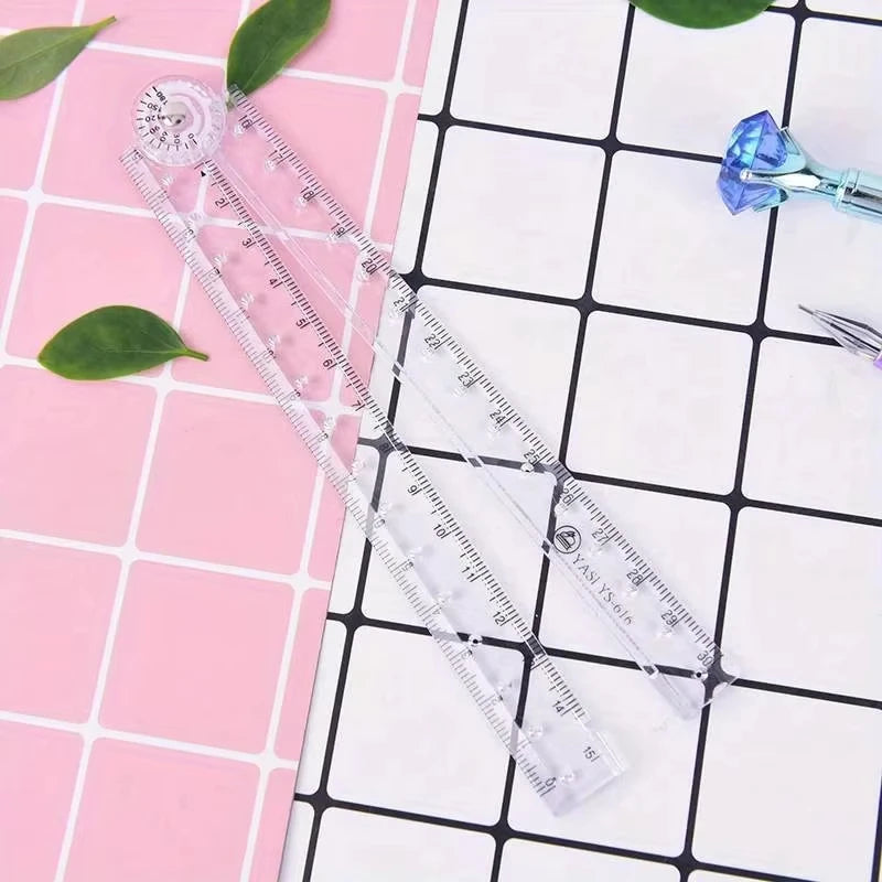A transparent foldable plastic ruler with markings is displayed on a pink and white grid background.
