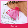 A pink rose red organza drawstring gift bag tied with a ribbon resting on a wooden surface.