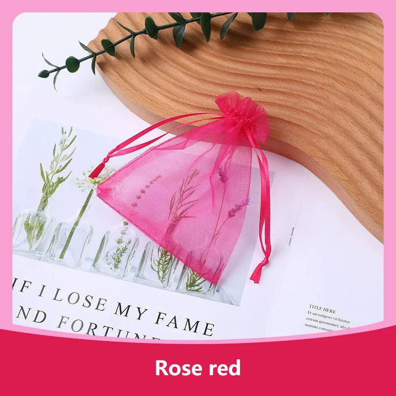 A pink rose red organza drawstring gift bag tied with a ribbon resting on a wooden surface.