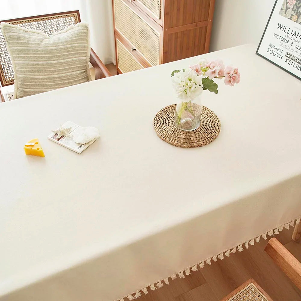 A white rectangular dining table covered with a cream tablecloth and decorated with floral arrangements and small yellow acce