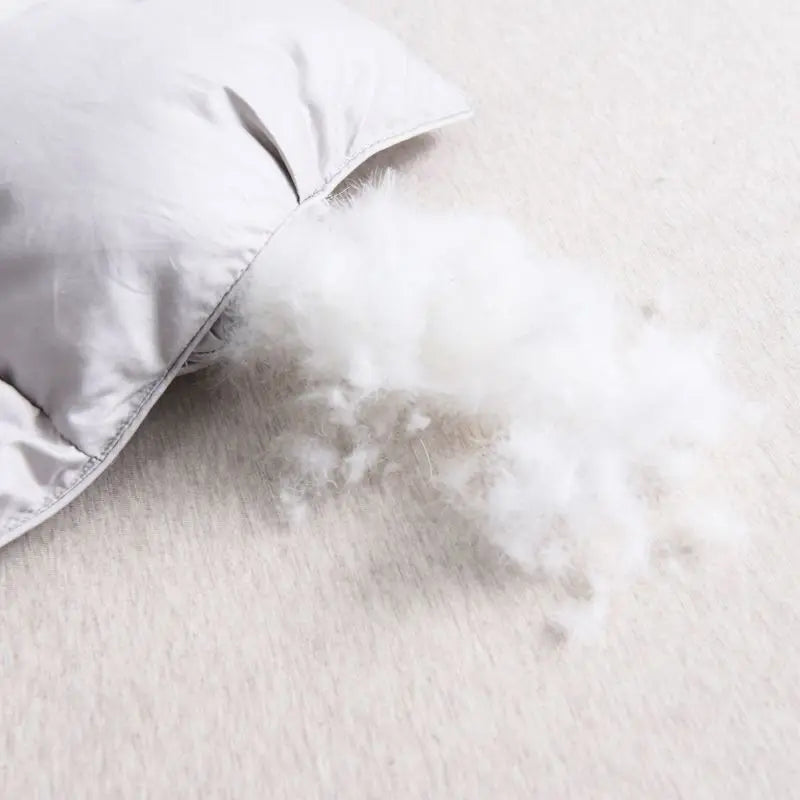 A close-up of a white goose down duvet with a cotton cover, showing fluffy white down spilling out onto a light surface.