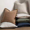 A stack of beige and olive green throw pillows with natural linen texture and fringe on a wooden surface.