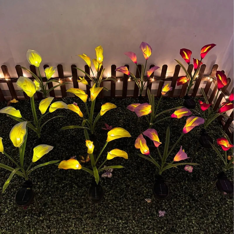 Yellow and pink calla lilies illuminated by solar-powered LED garden lights in a dark setting.