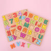 A wooden alphabet and number peg puzzle set showing various letters and numbers arranged on a light pink background.