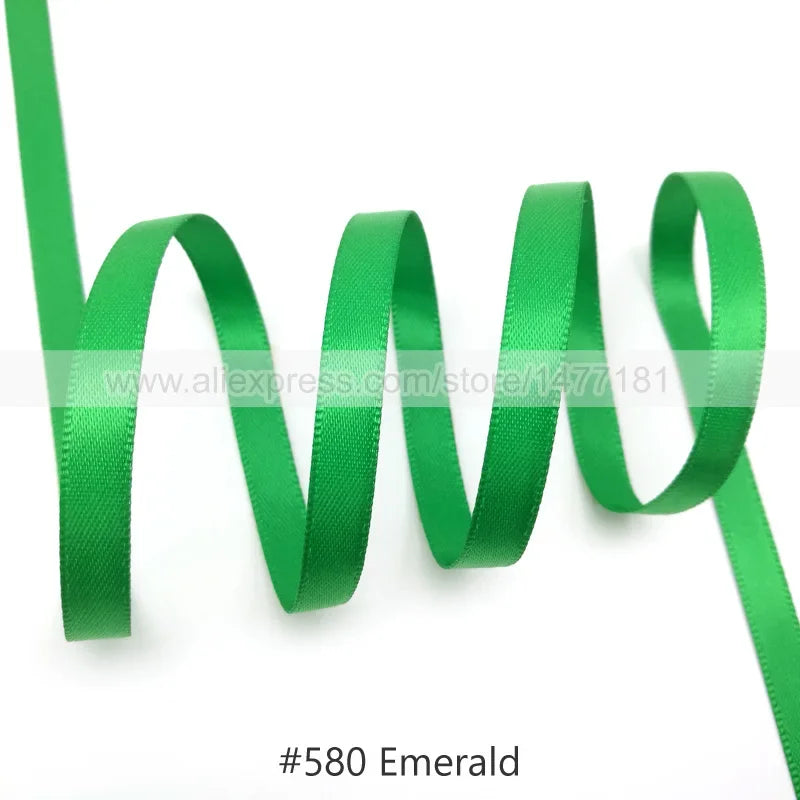 Green satin ribbon in an emerald color coiled and draped against a white background.