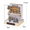 A wooden miniature coffee shop display featuring a counter, various cups and equipment, and an outdoor seating area.