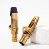 A gold-plated brass tenor saxophone mouthpiece with a black cap resting on a white surface.