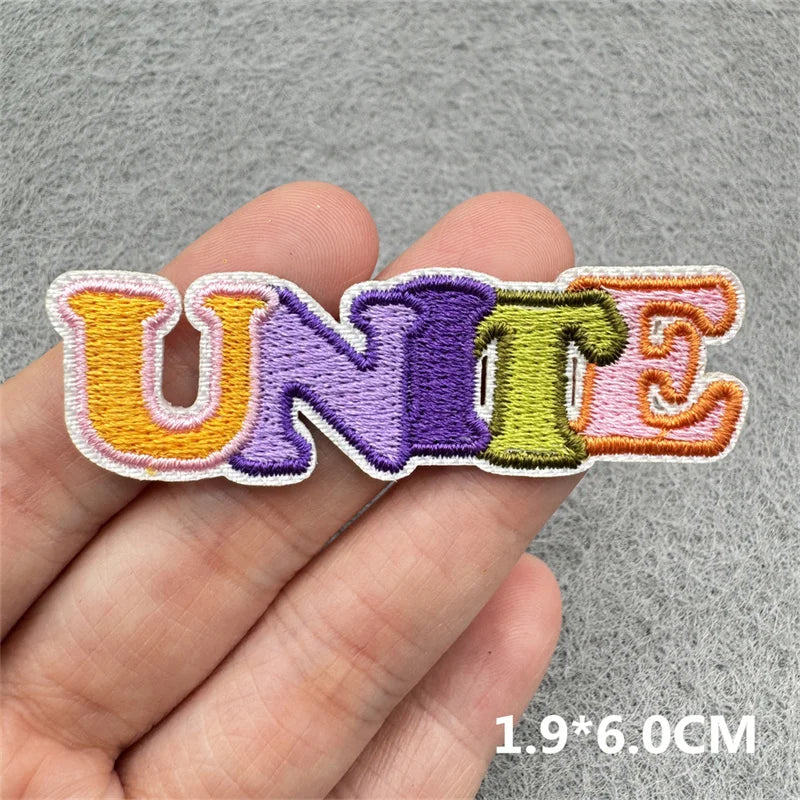 Embroidered iron-on patches spelling UNITE in various colors purple green orange and pink on a hand