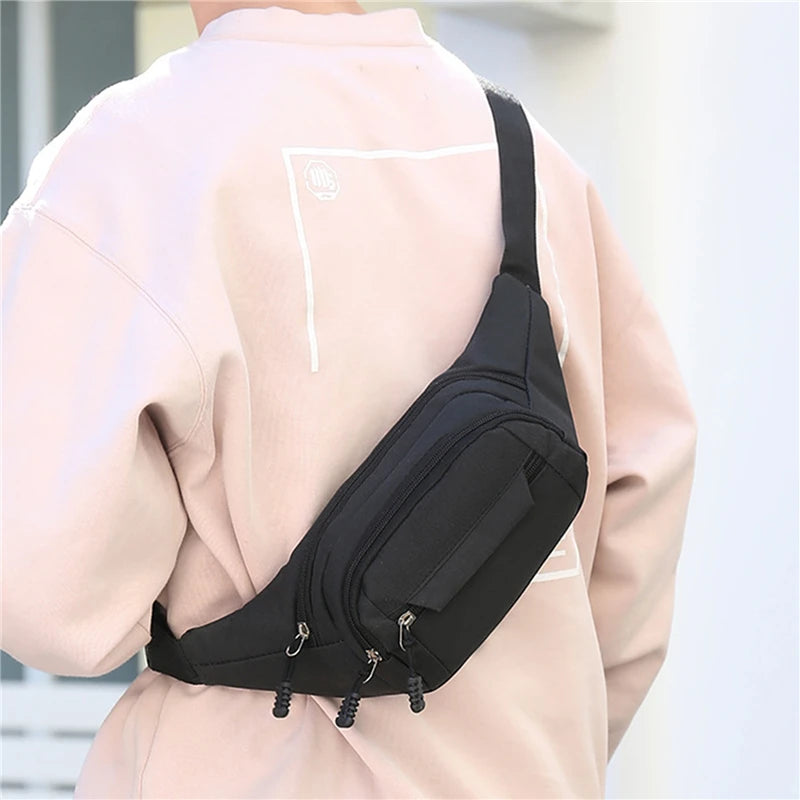 A close-up view of a black canvas waist pack worn on the back of a light pink jacket.