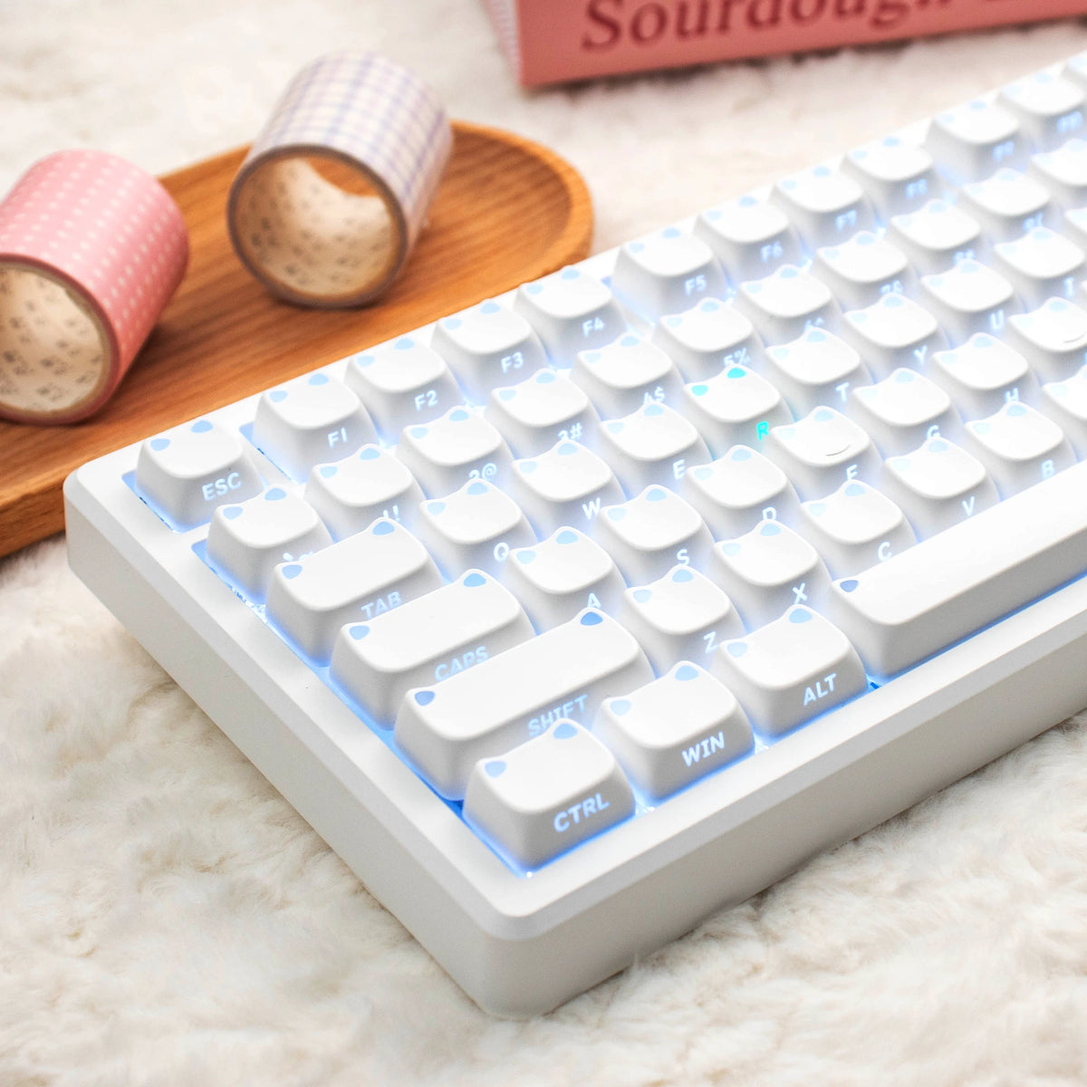 A close-up of a white mechanical keyboard with light blue backlit keys and a wooden surface featuring rolled keycaps.