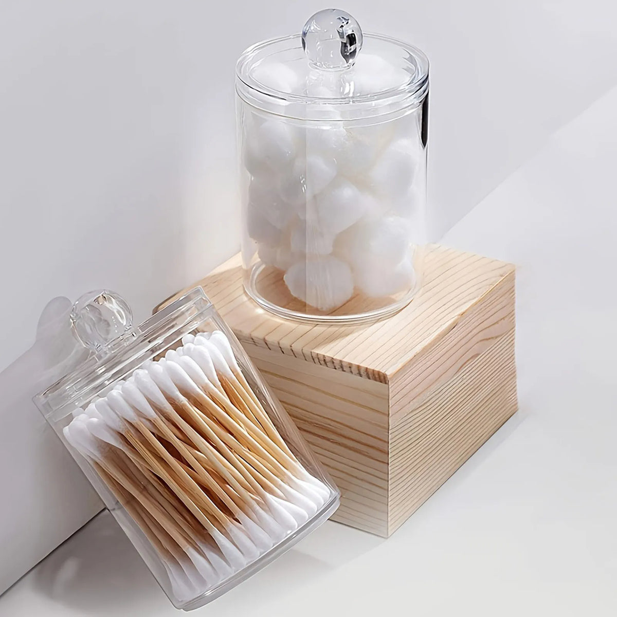 Clear storage jars with lids containing white cotton swabs and other small tools on a wooden block