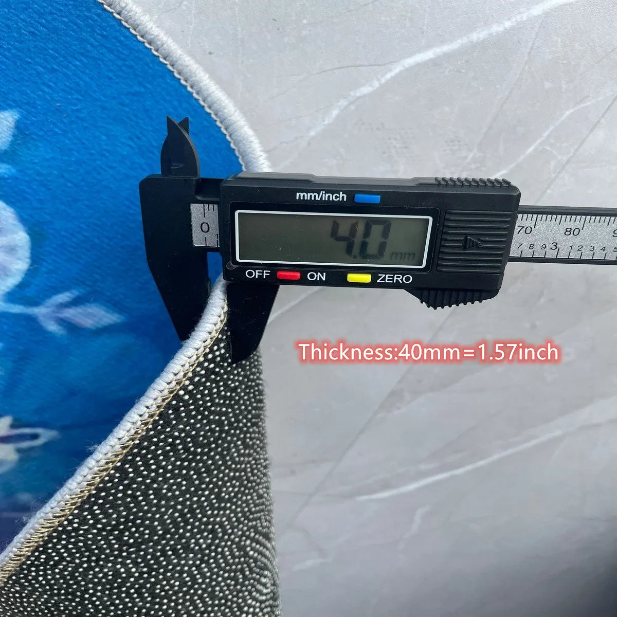 A digital caliper measures the thickness of a rug material, showing 40mm or 1.57 inches.