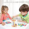Two children are playing with a wooden color sorting toy, arranging colorful sticks and blocks on a white table.