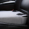 A gray ergonomic car seat cushion with a textured surface and black straps is placed on a black leather seat.