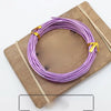 Purple anodized aluminum jewelry wire coiled on a wooden board with thin bamboo sticks.
