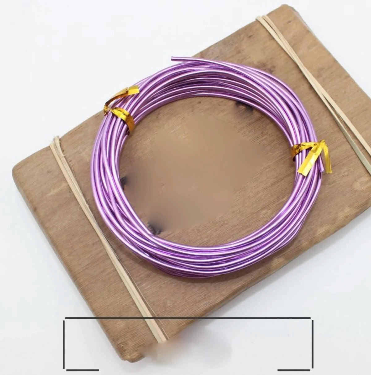 Purple anodized aluminum jewelry wire coiled on a wooden board with thin bamboo sticks.