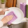 Hands are placing a purple reusable tear-away cleaning cloth onto a white plate in a kitchen setting.