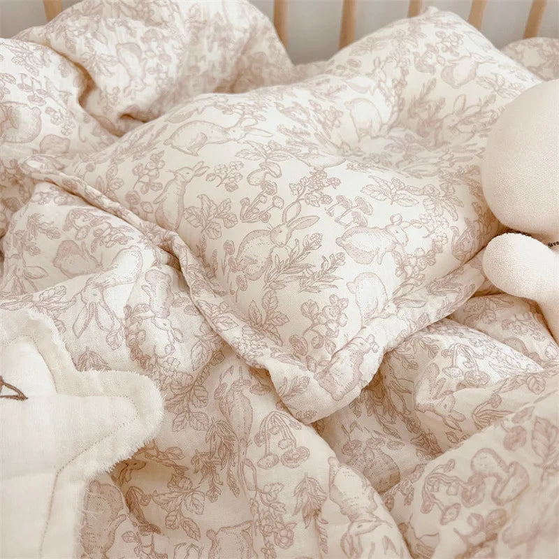 A close-up of a floral muslin baby blanket in beige and cream tones, folded and soft.