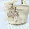A beige woven bag with a sheer lace charm featuring a sparkling starfish pendant.