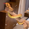 A hand is holding a lifelike, soft yellow snake plush toy with a red forked tongue.
