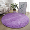 A round, purple, ultra-soft shaggy rug placed on a light wood floor in a living room setting.