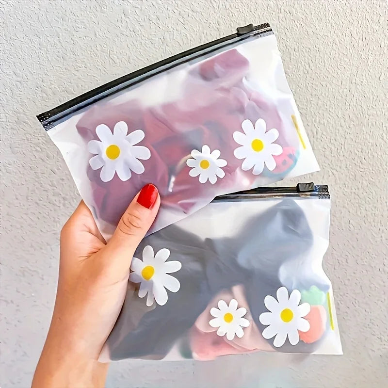 A hand holds a clear plastic zipper bag with a white daisy pattern, part of a set of reusable storage pouches.
