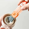 A hand is holding an orange multi-purpose cleaning brush set with a brush head and a container for cleaning bottles, cups, an