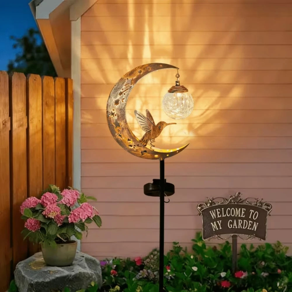 A solar owl garden light featuring a crescent moon silhouette and a bird design mounted on a wooden fence.