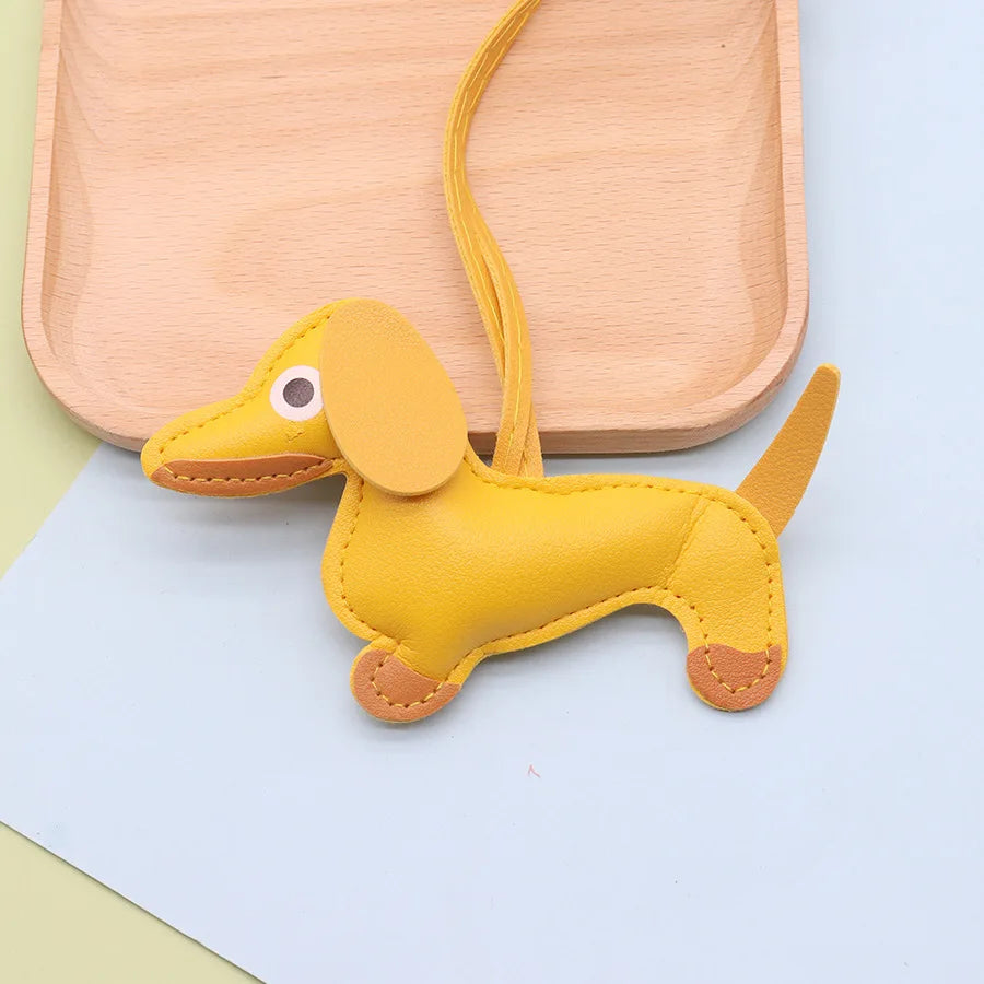 A yellow PU leather keychain shaped like a cute puppy with long ears and a tail, resting on a light wooden tray.