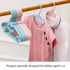 Pink and blue plastic hangers with bow designs for babies aged 0-12 hanging on a wooden rod.
