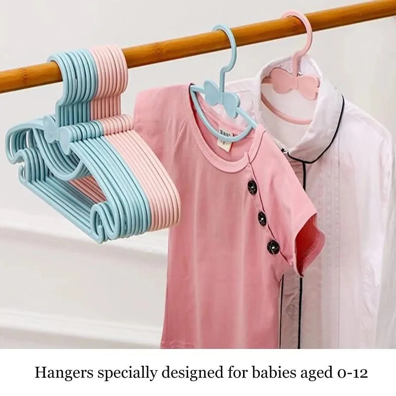 Pink and blue plastic hangers with bow designs for babies aged 0-12 hanging on a wooden rod.